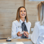 Recepcionista en el front desk de un hotel ofrece una llave al huésped tras haber realizado el proceso de pre-estancia en hoteles.